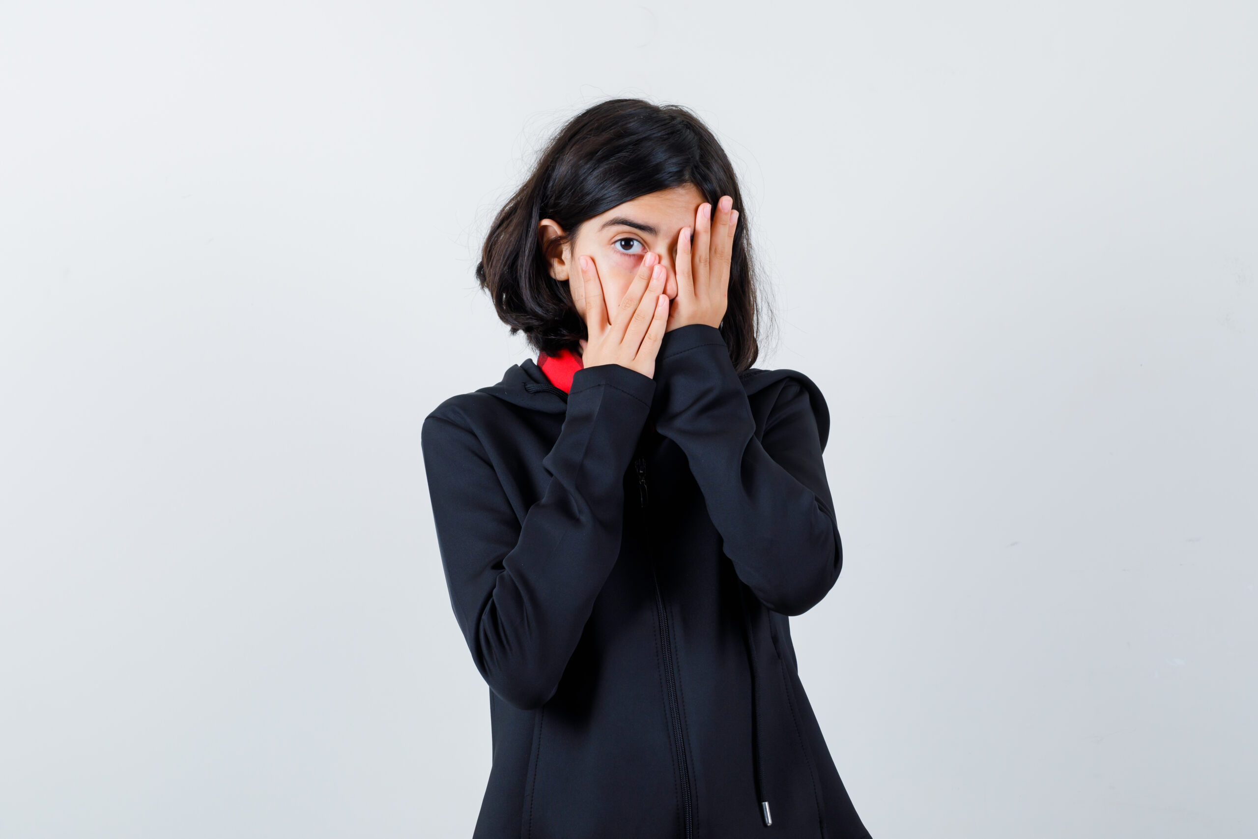Little Girl Looking Through Fingers In Black Coat And Looking Scared , Front View.