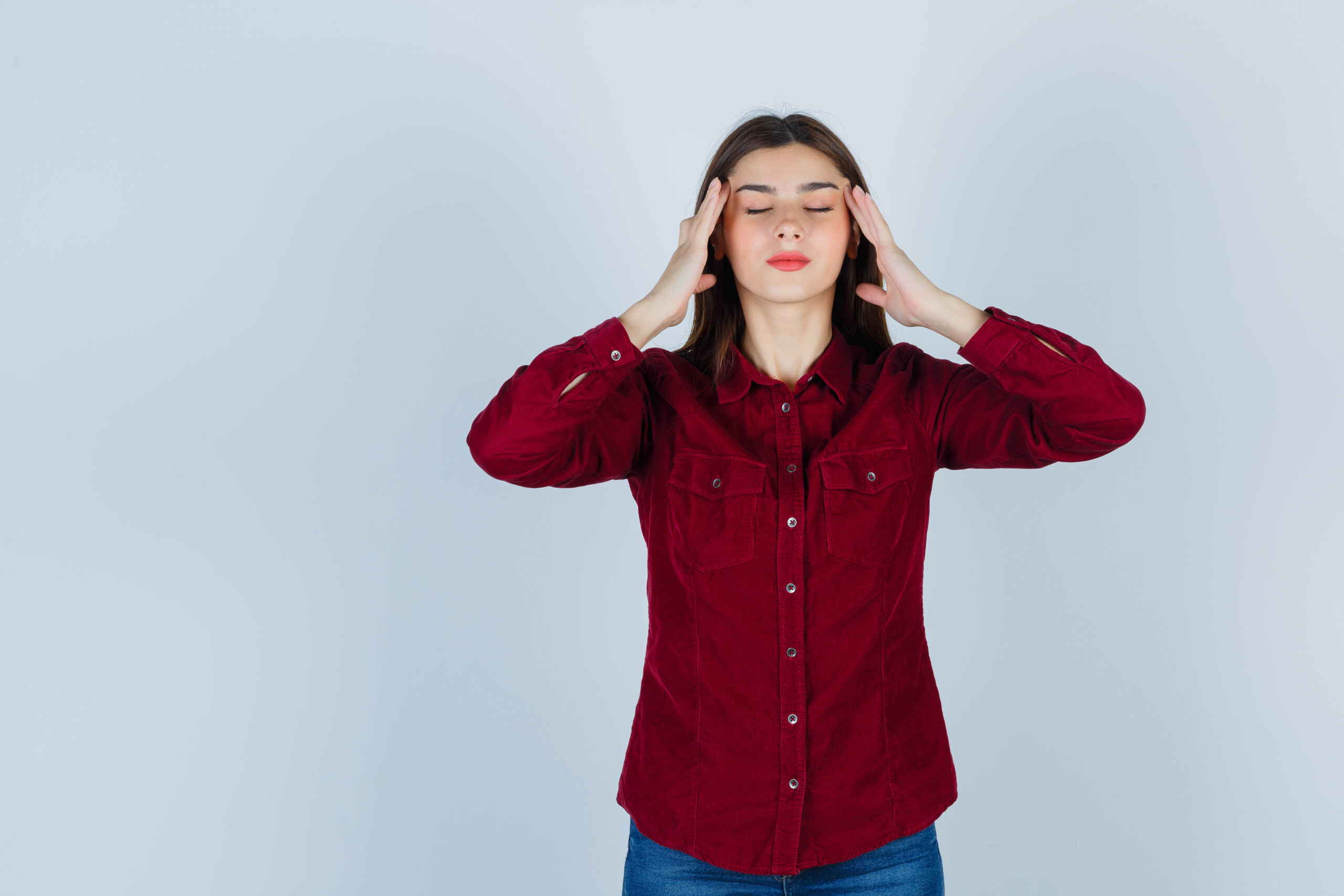 Teenage Girl Rubbing Temples In Burgundy Shirt And Looking Relaxed. Front View.